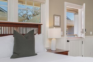 Un dormitorio con cama, almohadas, mesita de noche, lámpara y ventana.