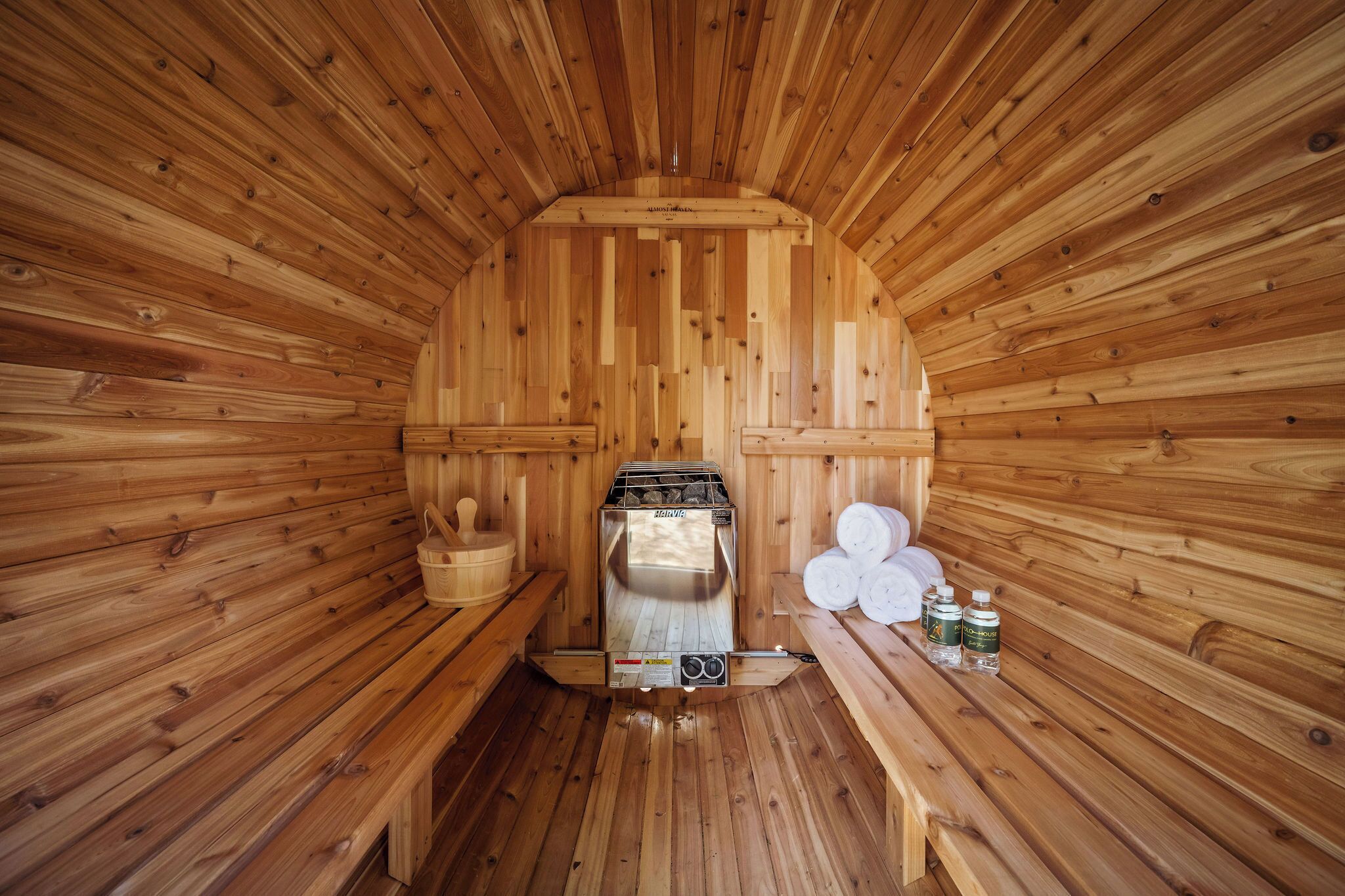 A sauna with wooden walls and benches, a sauna heater, and some towels and bottles on the benches.
