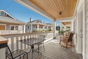 A covered outdoor patio with a table and chairs, a wooden deck, and a white fence.