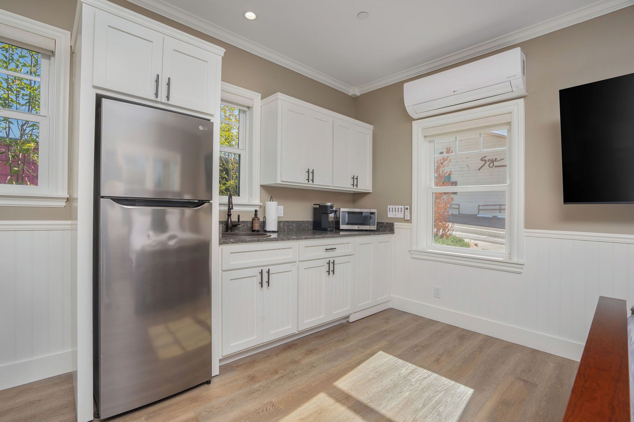 Una cocina moderna con armarios blancos, un refrigerador de acero inoxidable, un microondas y un televisor de pantalla plana montado en la pared.