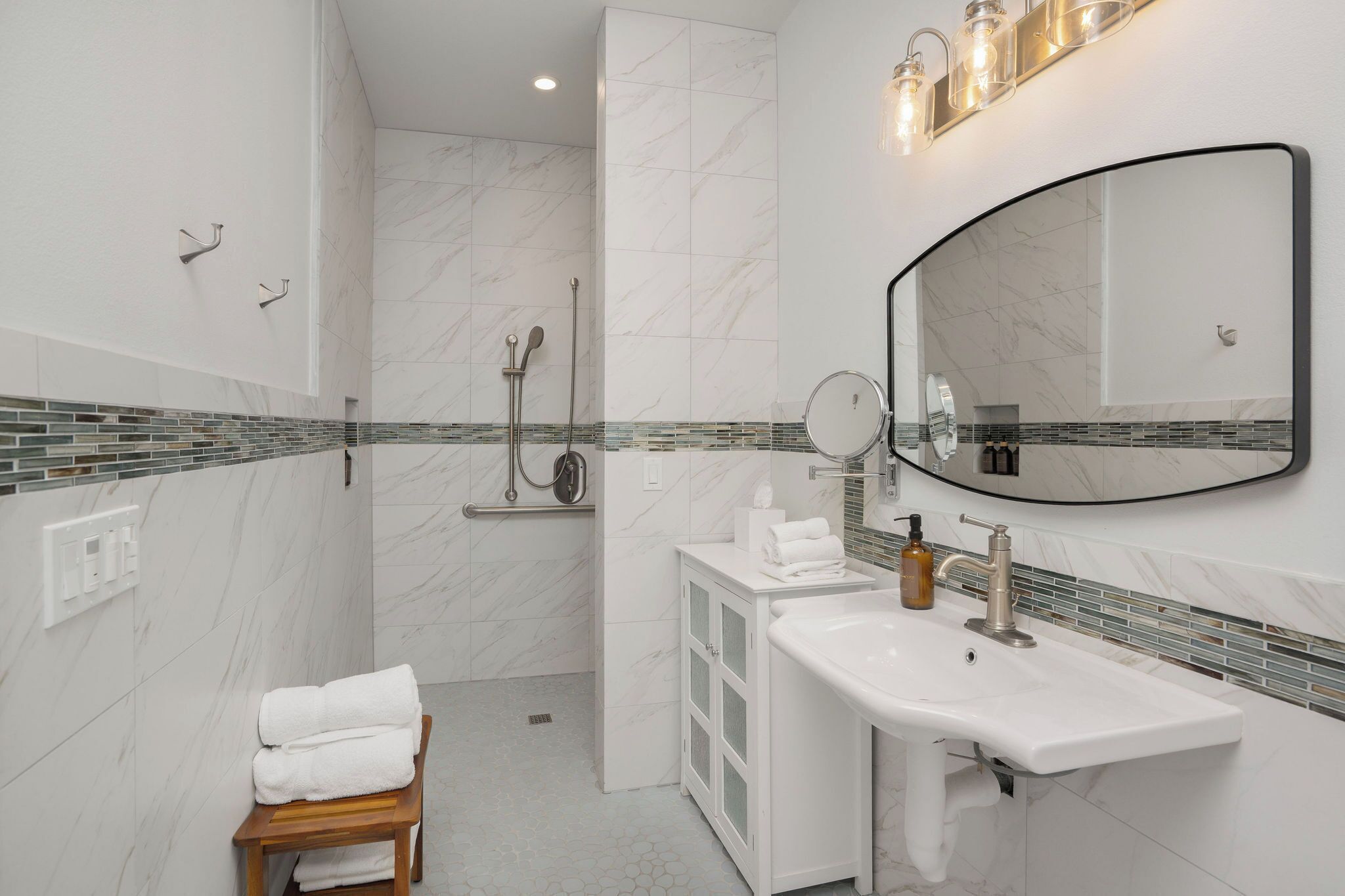 A modern bathroom with a white sink, mirror, and shower area.