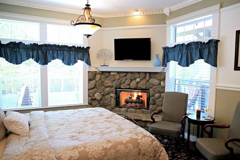 Une chambre avec une cheminée en pierre, un lit recouvert d’une couvre-lit à motifs floraux, un téléviseur fixé au mur et deux fauteuils.