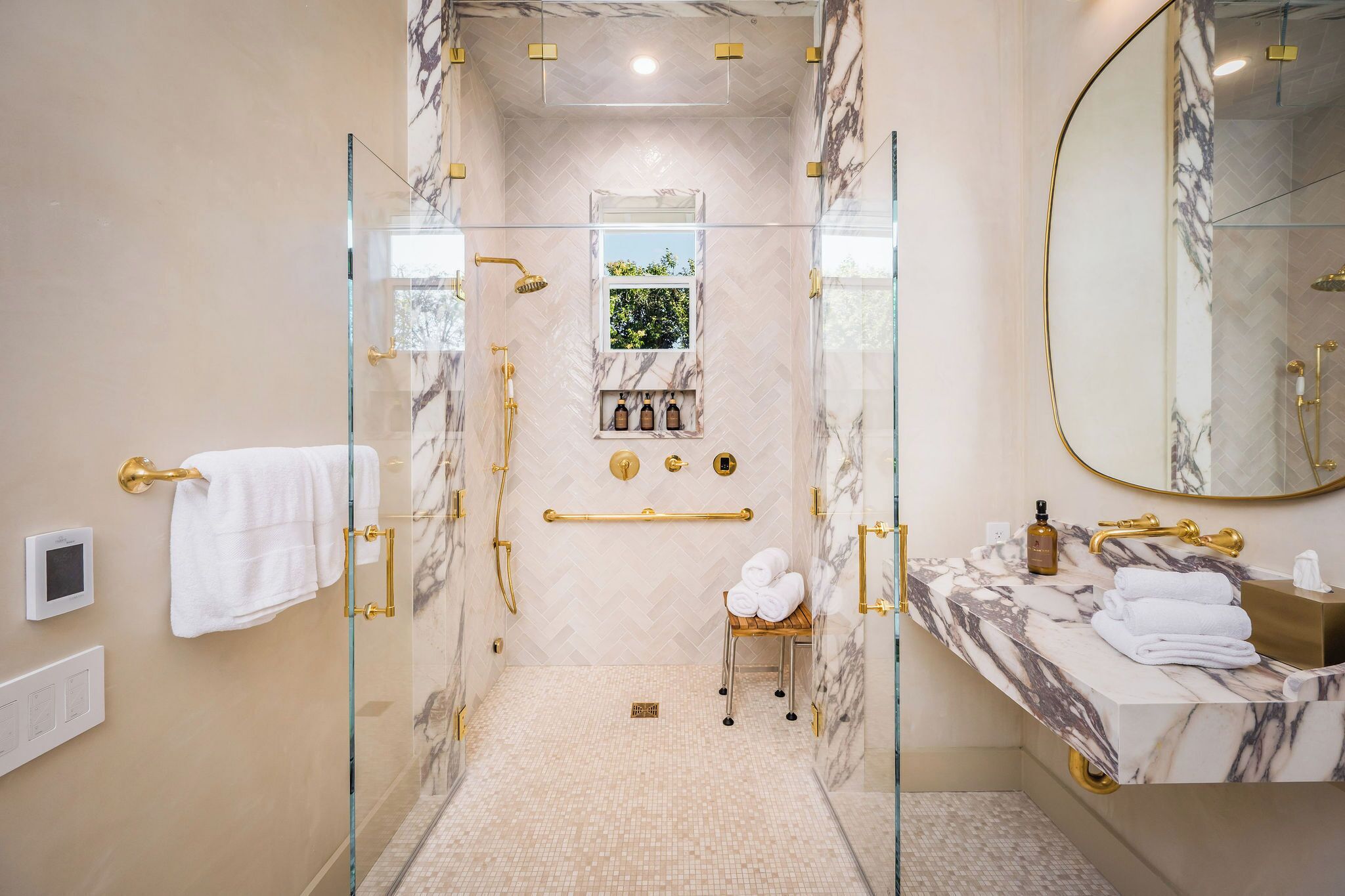 A bathroom with a glass-enclosed shower, marble walls, a vanity with a sink, and a large mirror.