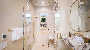 A bathroom with a glass-enclosed shower, marble walls, a vanity with a sink, and a large mirror.