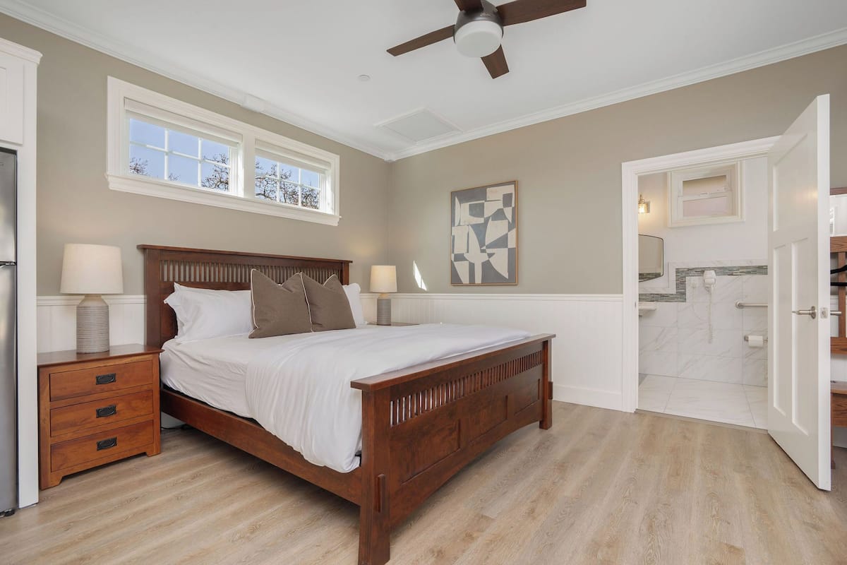 A bedroom with a wooden bed, bedside tables, a ceiling fan, and a bathroom visible through an open door.