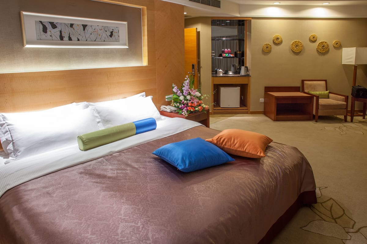 Quarto de hotel com uma cama grande, uma mesa, uma cadeira e um pequeno frigorífico.
