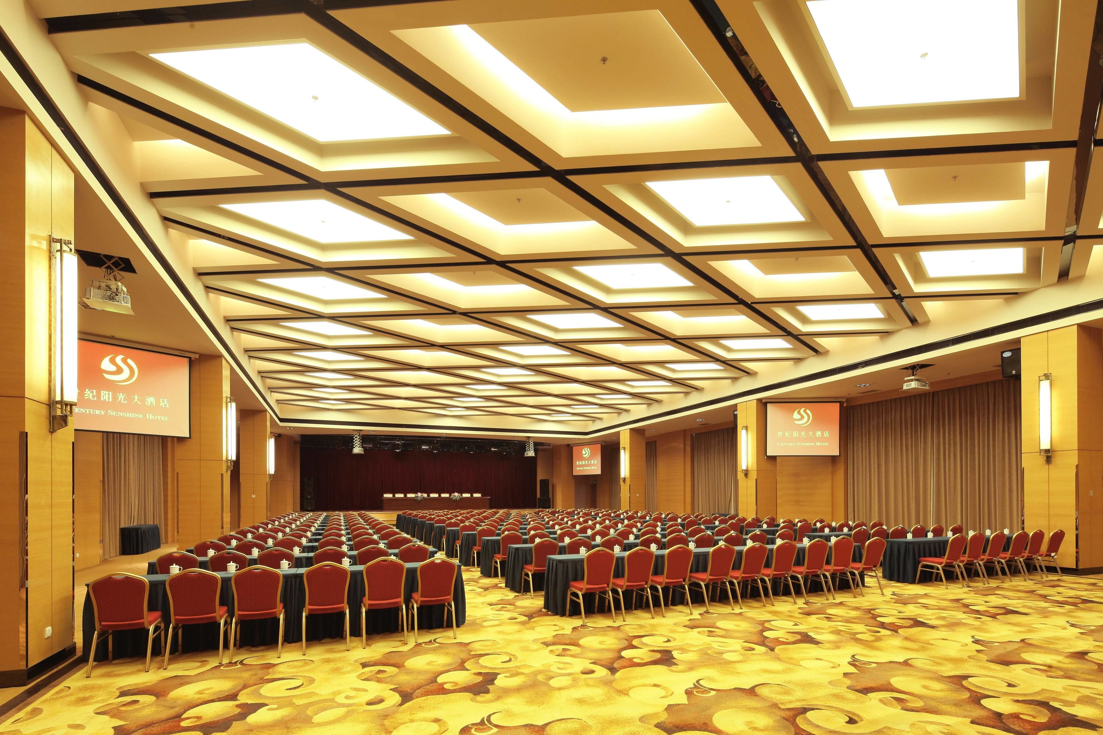 A conference room with rows of tables and chairs, a stage, and a large screen.