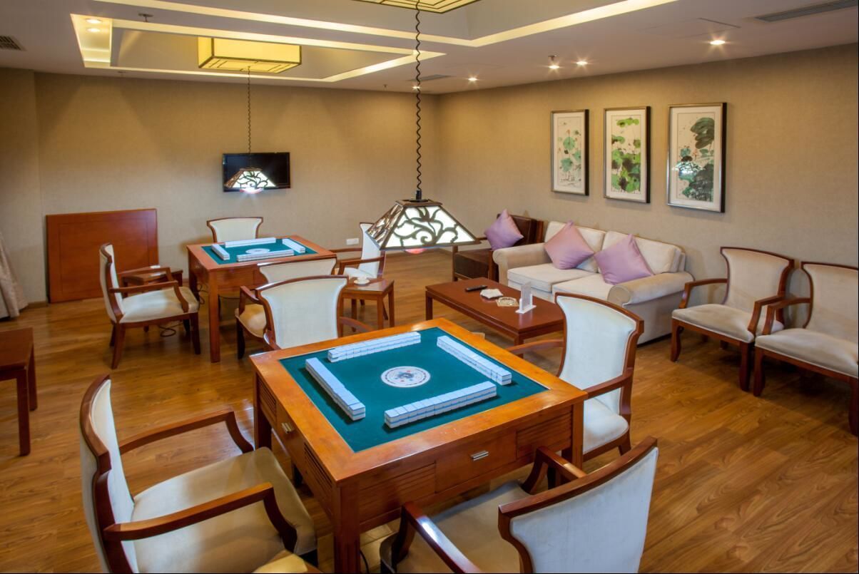 A well-lit room with a wooden table, chairs, a sofa, and a TV mounted on the wall.