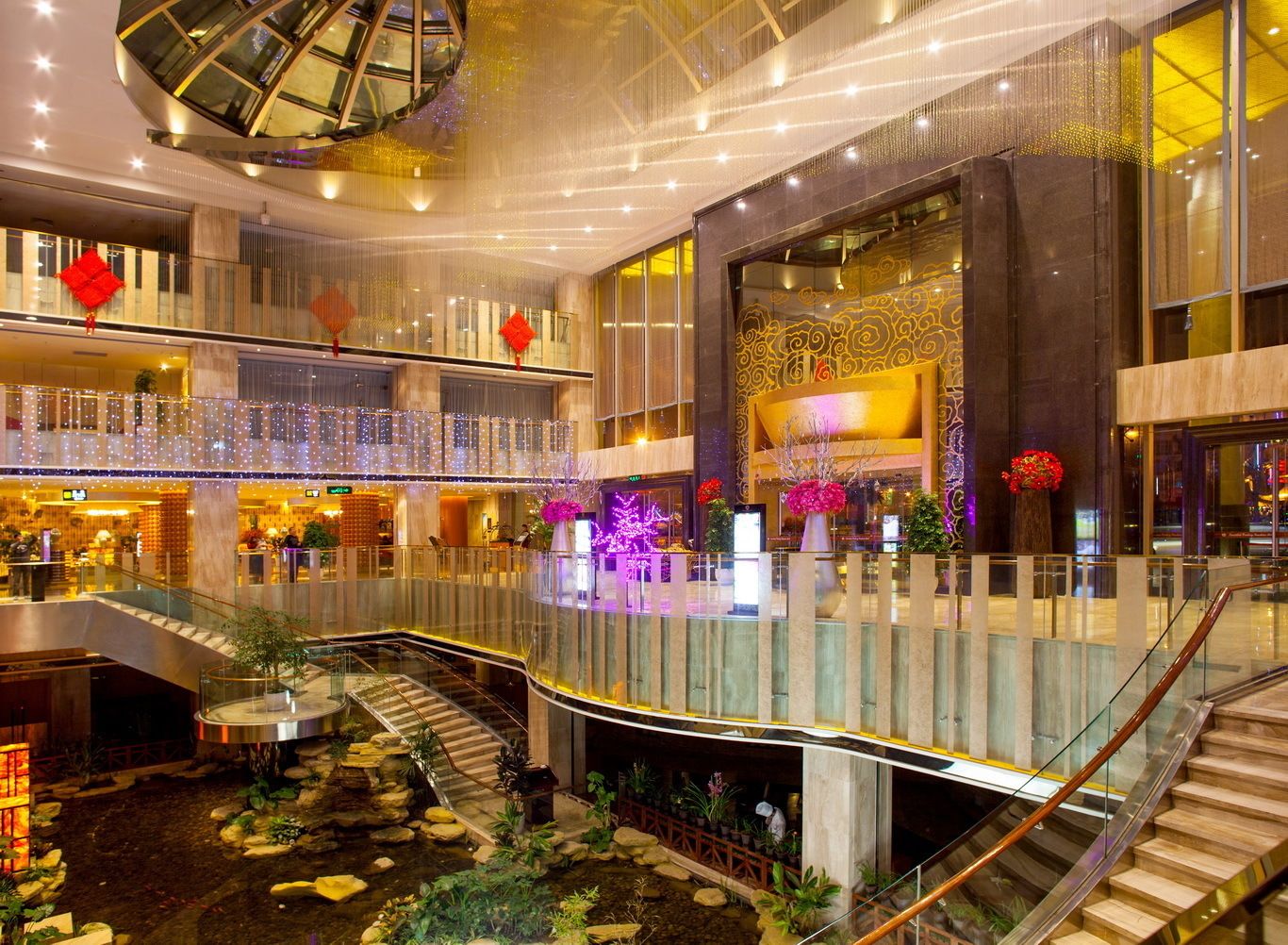 A multi-level indoor space with a central atrium, glass railings, and a water feature.