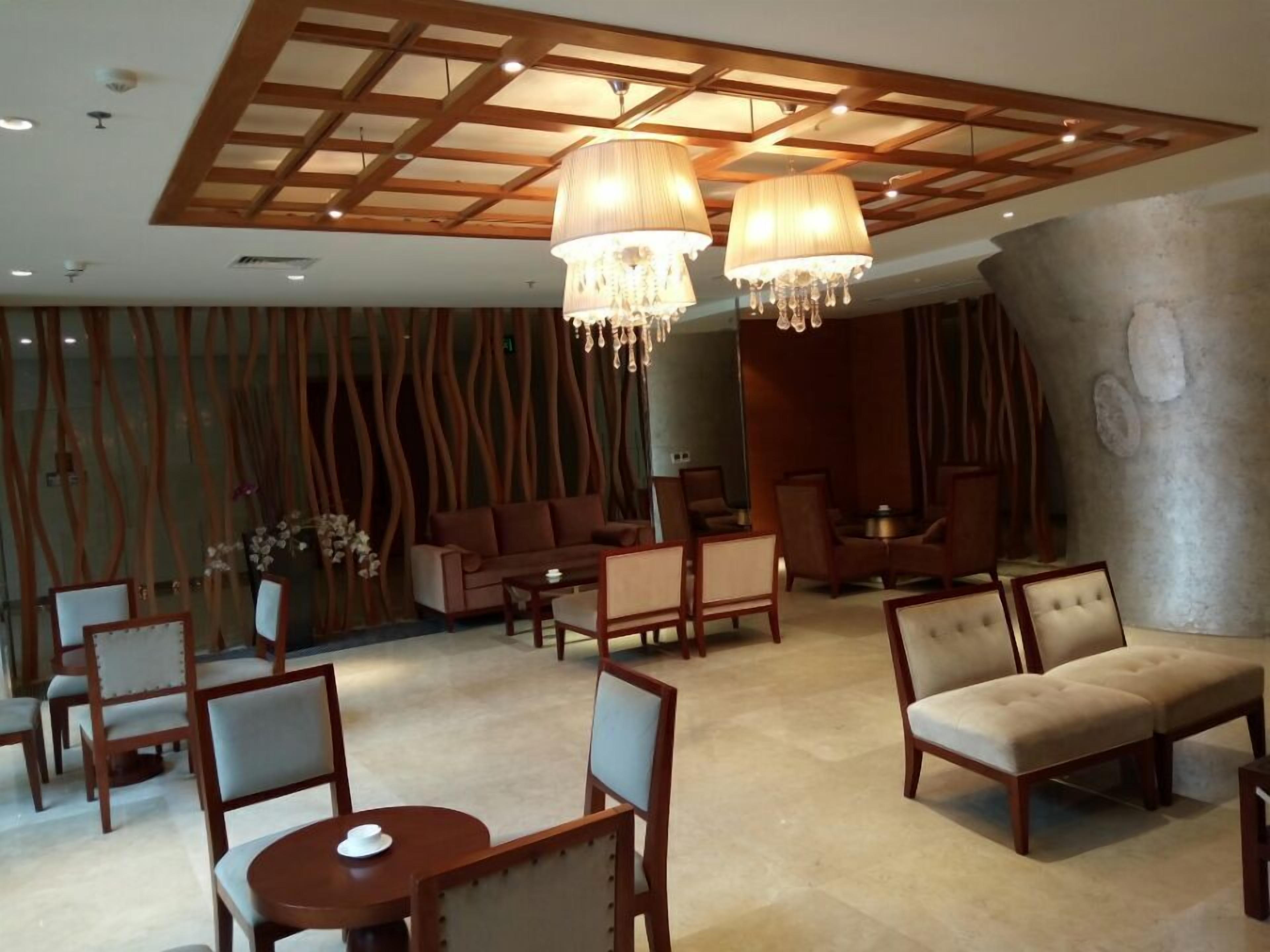 Un vestíbulo espacioso con techo alto, vigas de madera y candelabros. Hay varias zonas de estar con sofás y sillones, y una mesa redonda con una taza.