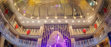 A multi-level atrium with a glass ceiling, wooden railings, and a central illuminated tree structure.