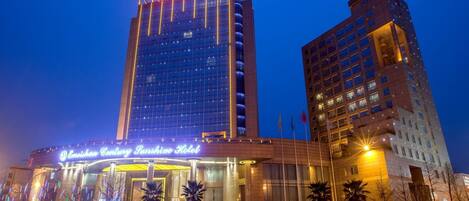 A hotel with a modern glass facade, a prominent sign, and a well-lit entrance.
