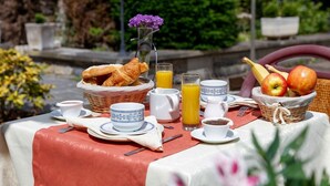 Mesa de desayuno al aire libre con cruasanes, fruta, jugo y café.