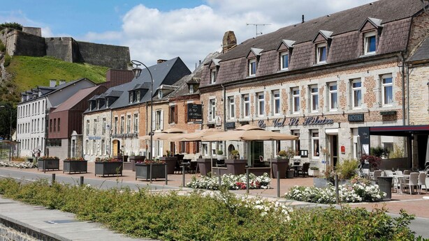 Un hotel con terraza al aire libre, un cartel que dice 'Hotel de Ville' y un muro de piedra al fondo.