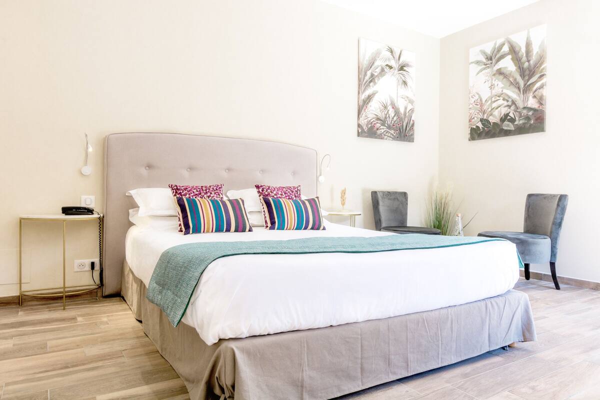 Quarto bem arrumado com uma cama grande, mesas de cabeceira, uma cadeira e quadros nas paredes.