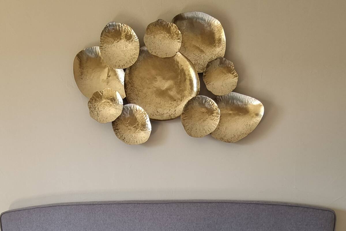 Uma cama com lençóis brancos, cabeceira estofada cinza e um objeto decorativo na parede acima.