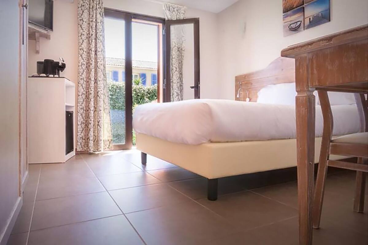Quarto com cama, cadeira de madeira, escrivaninha e janela com cortinas.