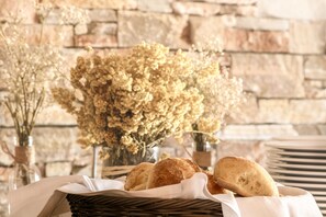 Una cesta de pan sobre una mesa con un fondo de pared de piedra y flores secas.