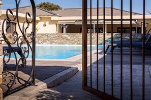 Zona de piscina con pared de piedra, una reja metálica y sillones de descanso.