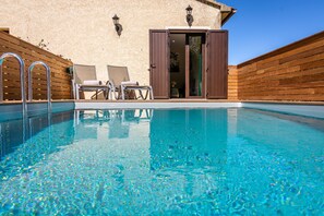Una piscina con dos sillas de descanso y una terraza de madera.