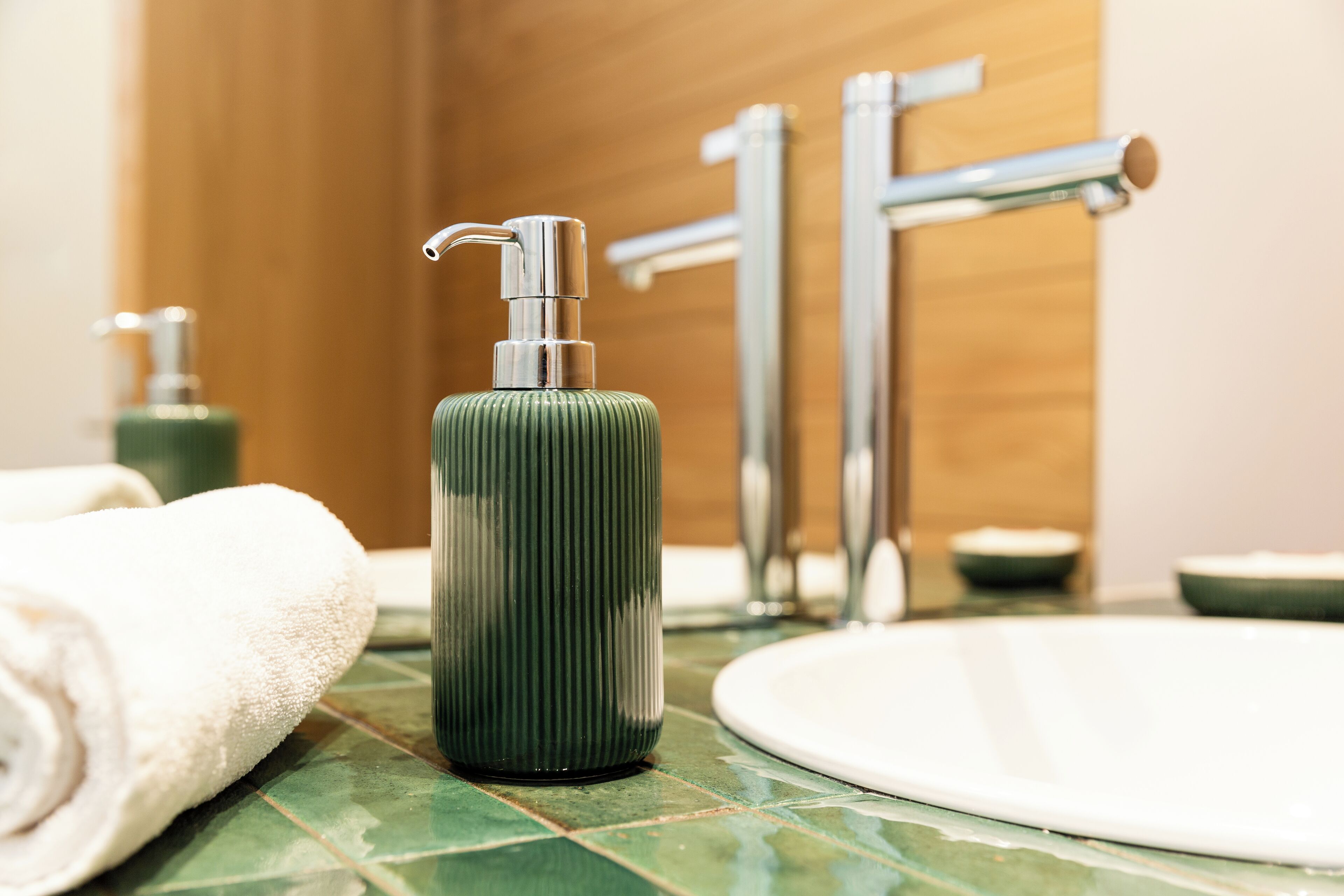 A bathroom with a green tiled sink, a white towel, and a green bottle of soap.