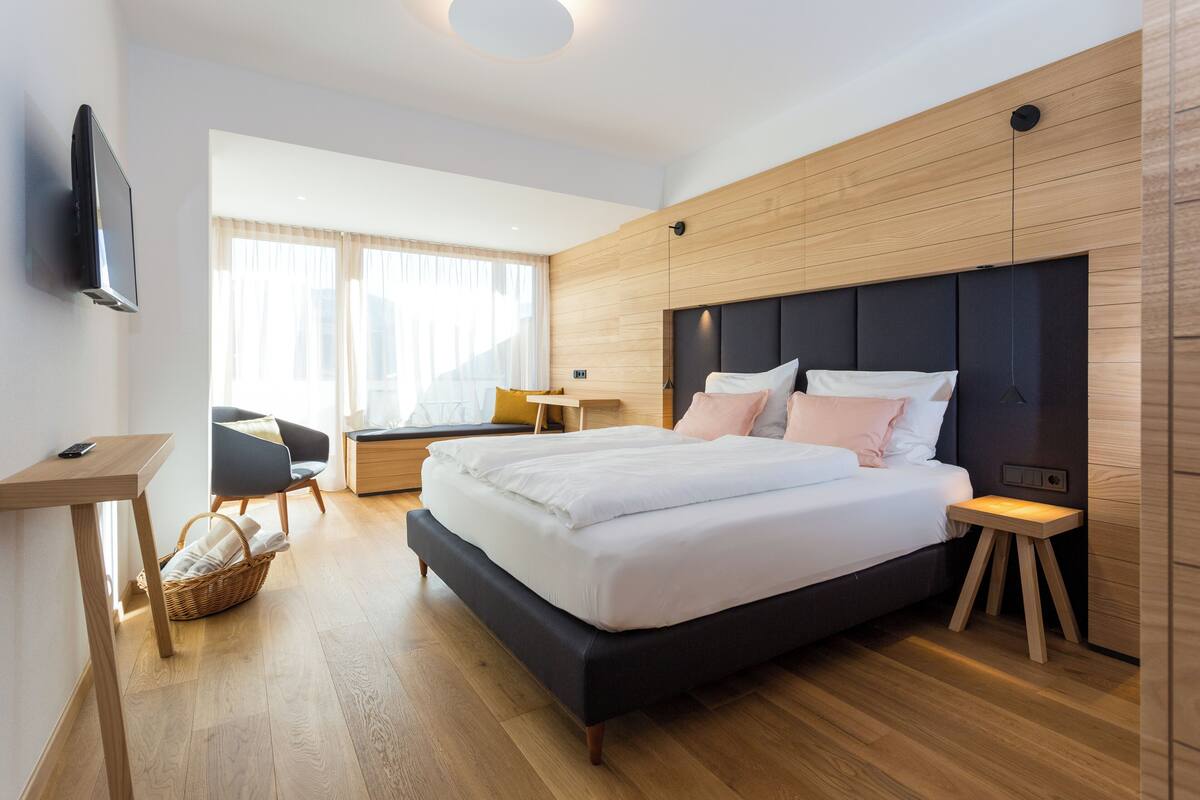 A modern hotel room with a large bed, a desk, a chair, and a TV.