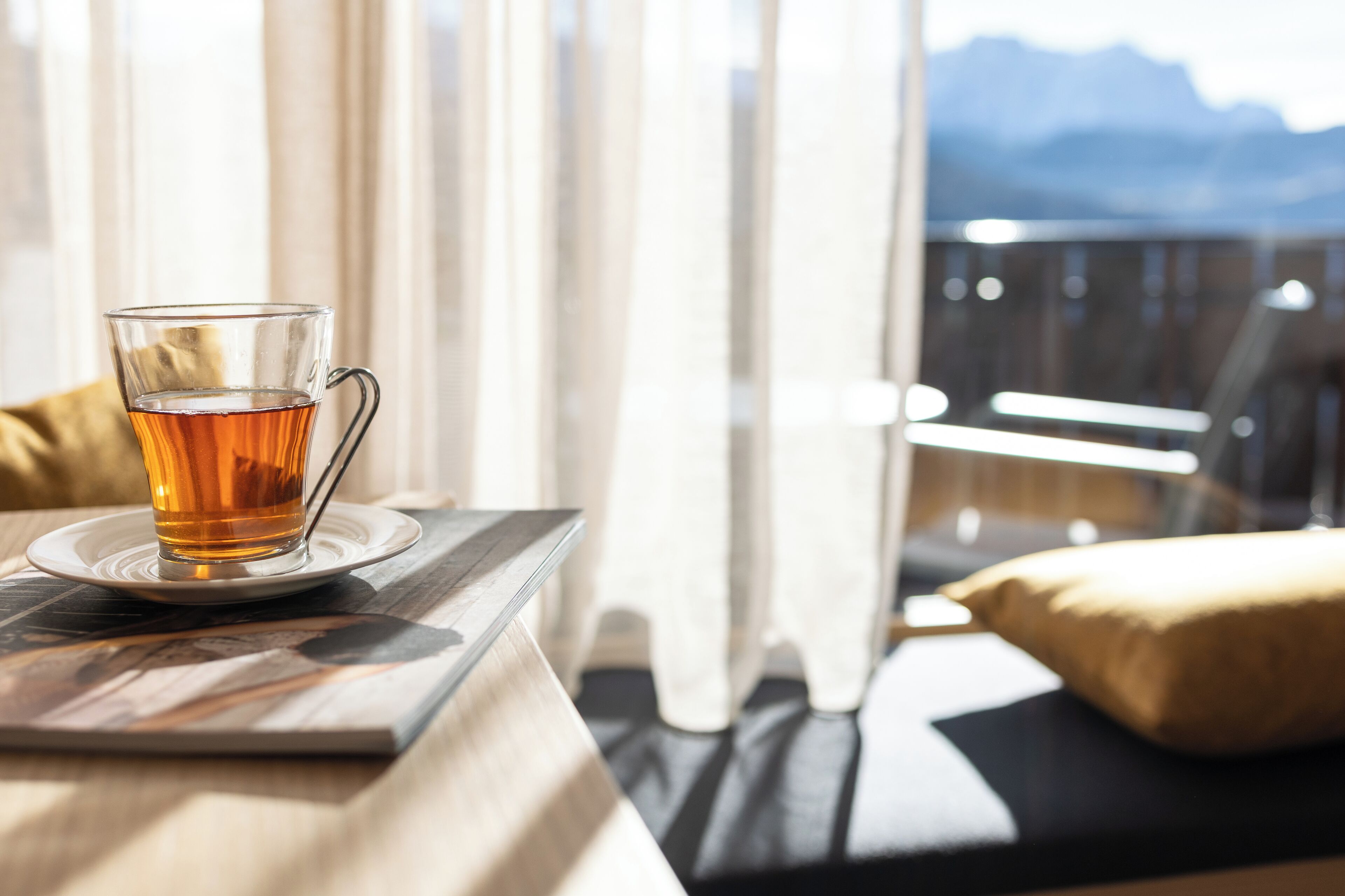Una taza de té sobre un platito en una mesa al lado de una ventana con vistas a montañas.