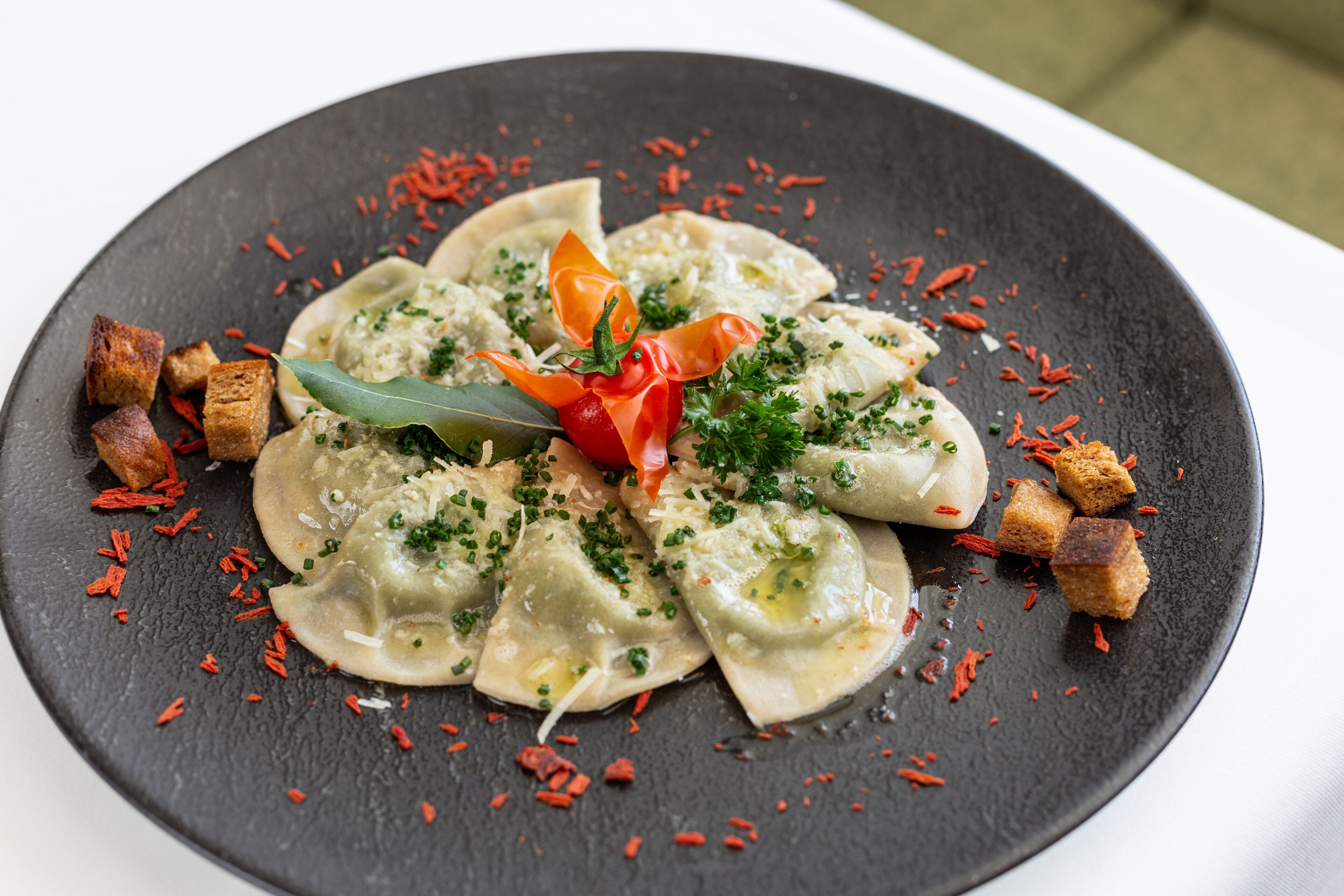 Een bord ravioli, versierd met kruiden en rode vlokken, geserveerd op een donker leisteenbord.