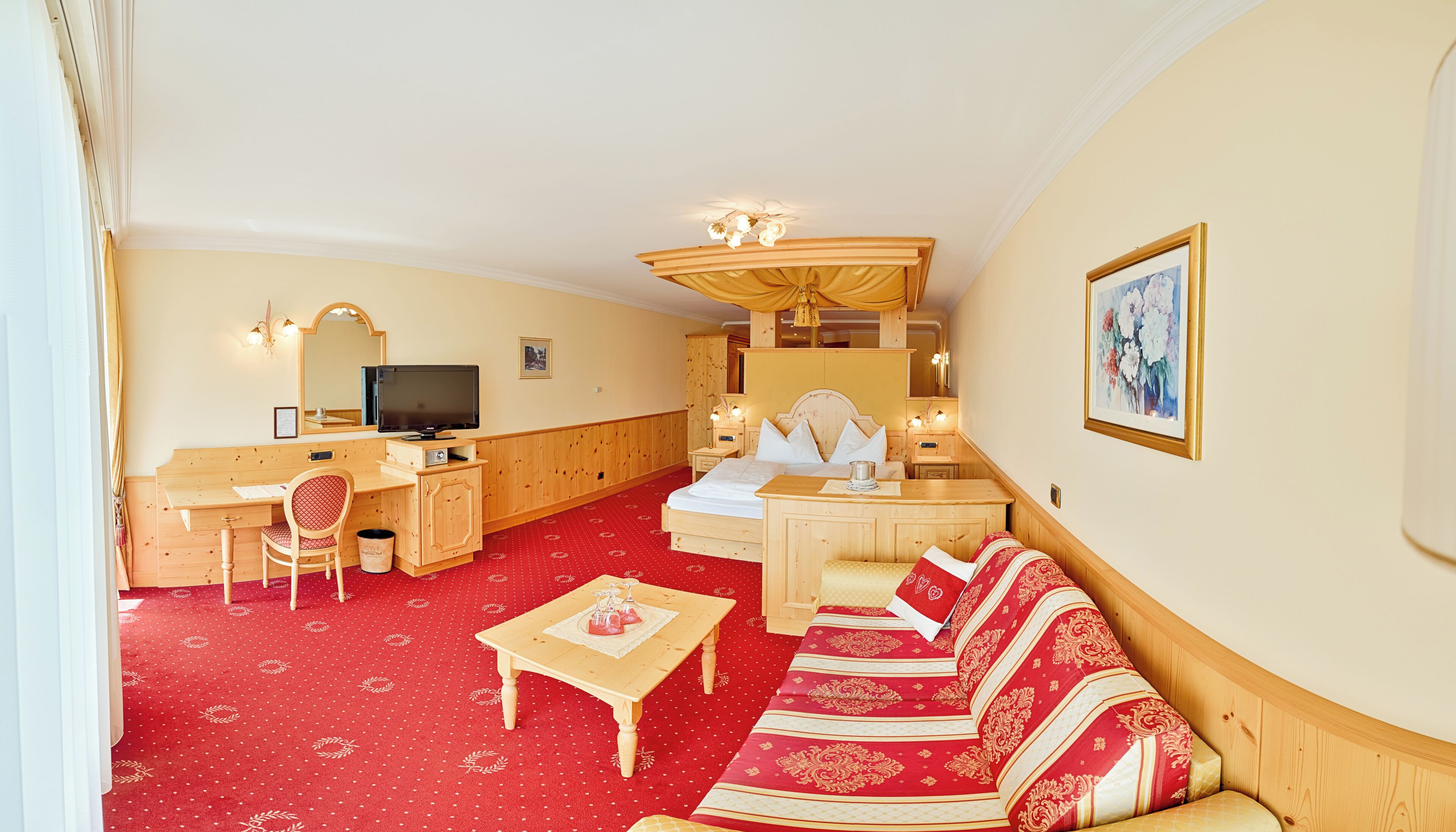 A hotel room with a bed, a desk, a chair, a sofa, and a television.