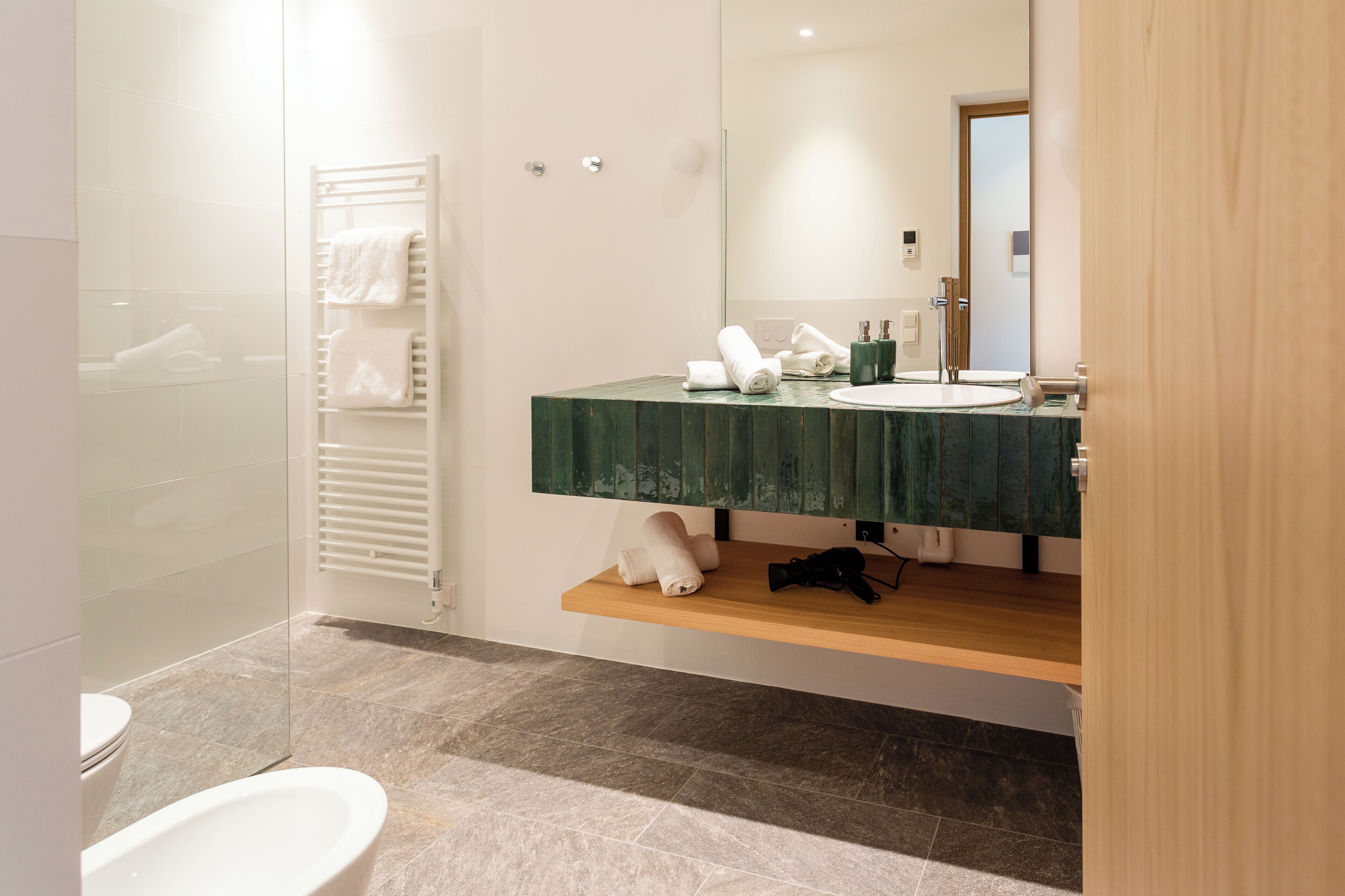 A modern bathroom with a glass shower enclosure, a white toilet, a wooden vanity with a green marble countertop, and a mirror above the sink.