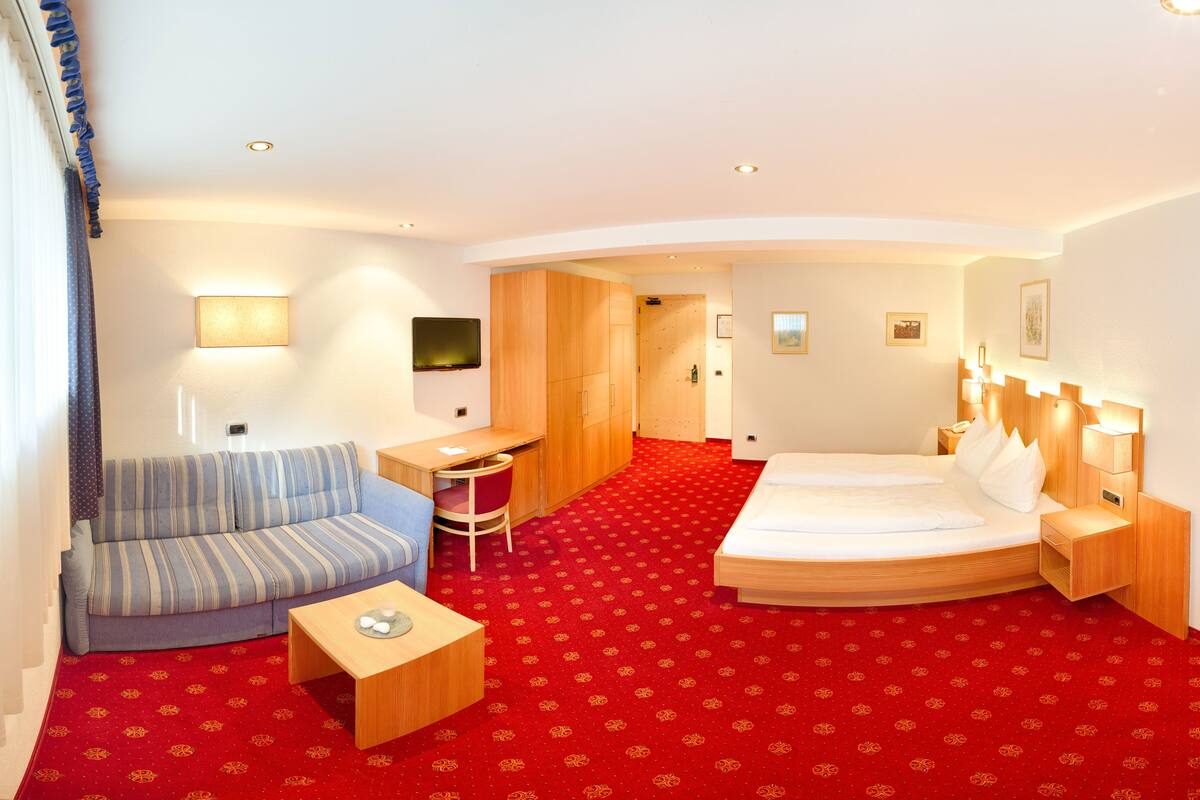 A hotel room with a bed, a sofa, a desk, and a TV.