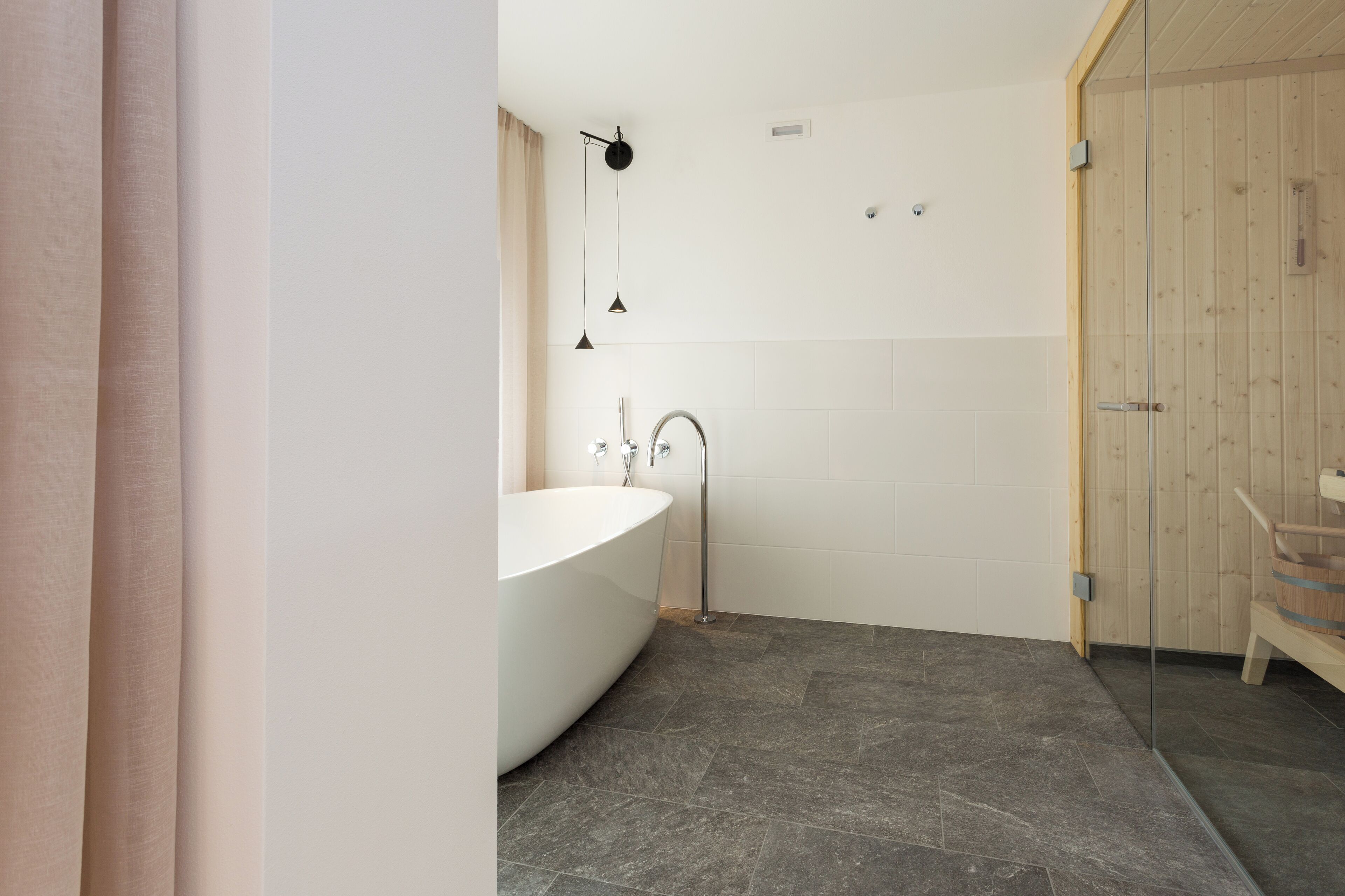 A modern bathroom with a freestanding bathtub, a glass shower enclosure, and a wooden door.