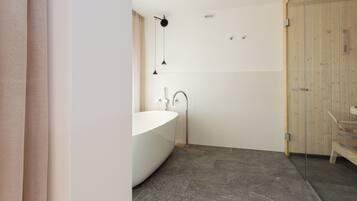 A modern bathroom with a freestanding bathtub, a glass shower enclosure, and a wooden door.