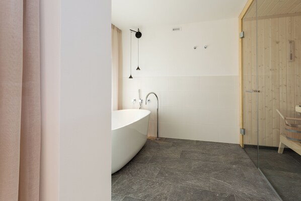 Un baño moderno con una bañera independiente, cabina de ducha con paredes de cristal y una puerta de madera.