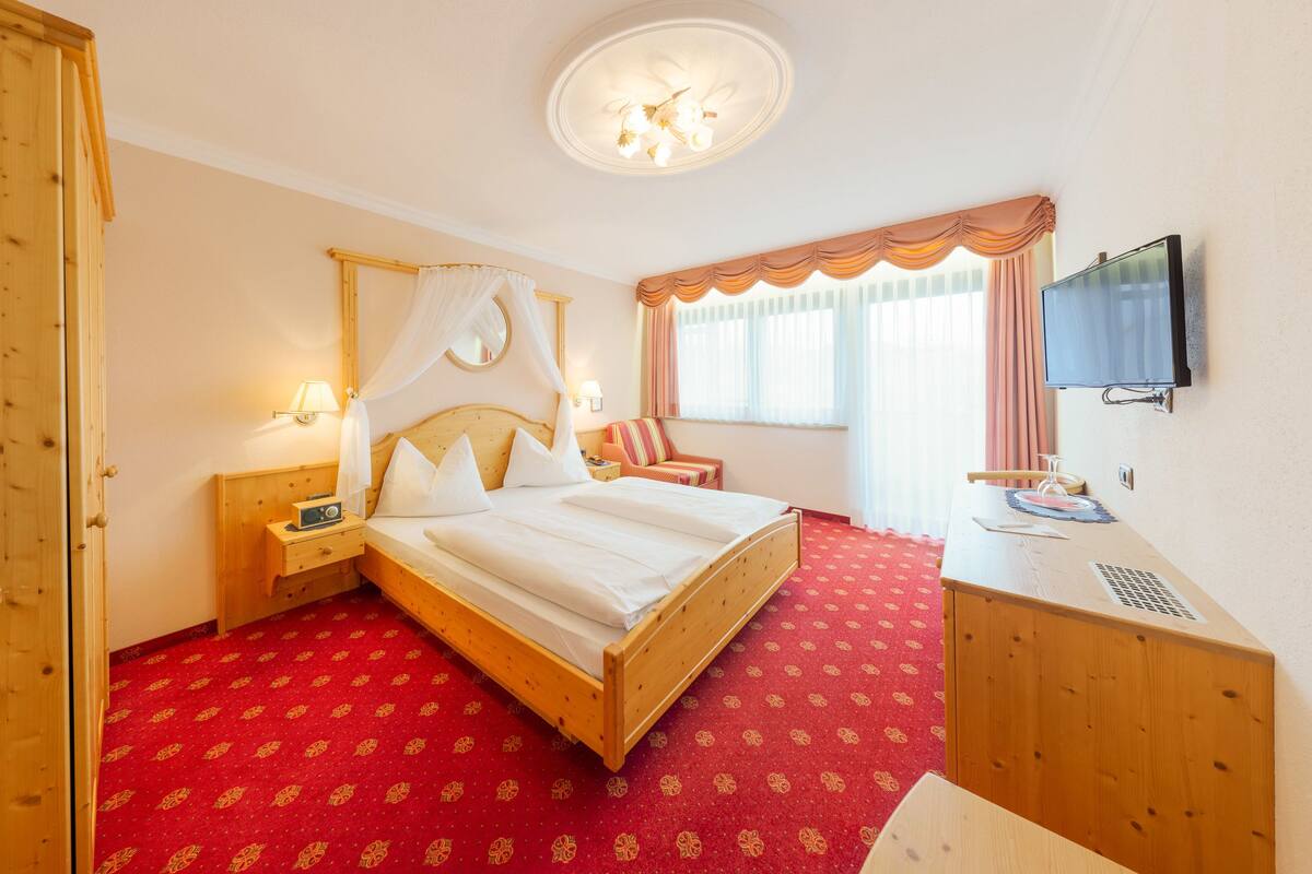 A hotel room with a wooden bed, a desk with a television, a chair, and a window with curtains.