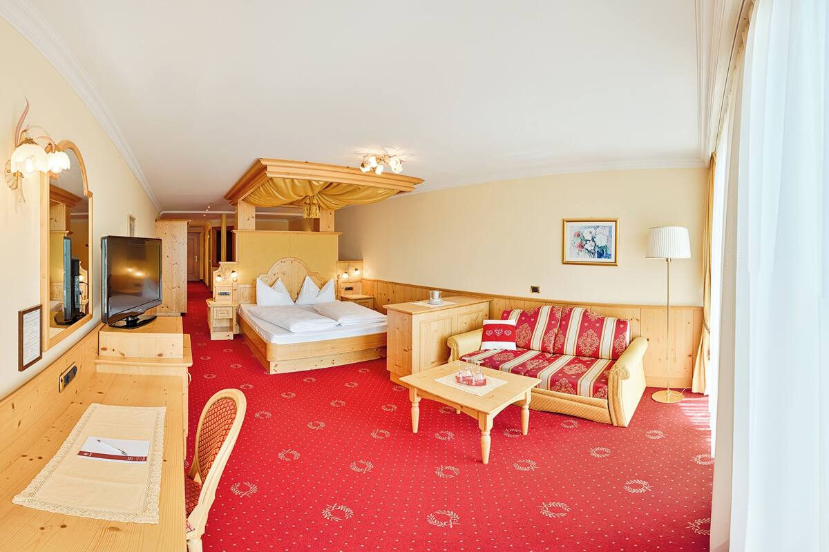 A hotel room with a wooden bed, a red patterned sofa, a wooden desk, and a television.