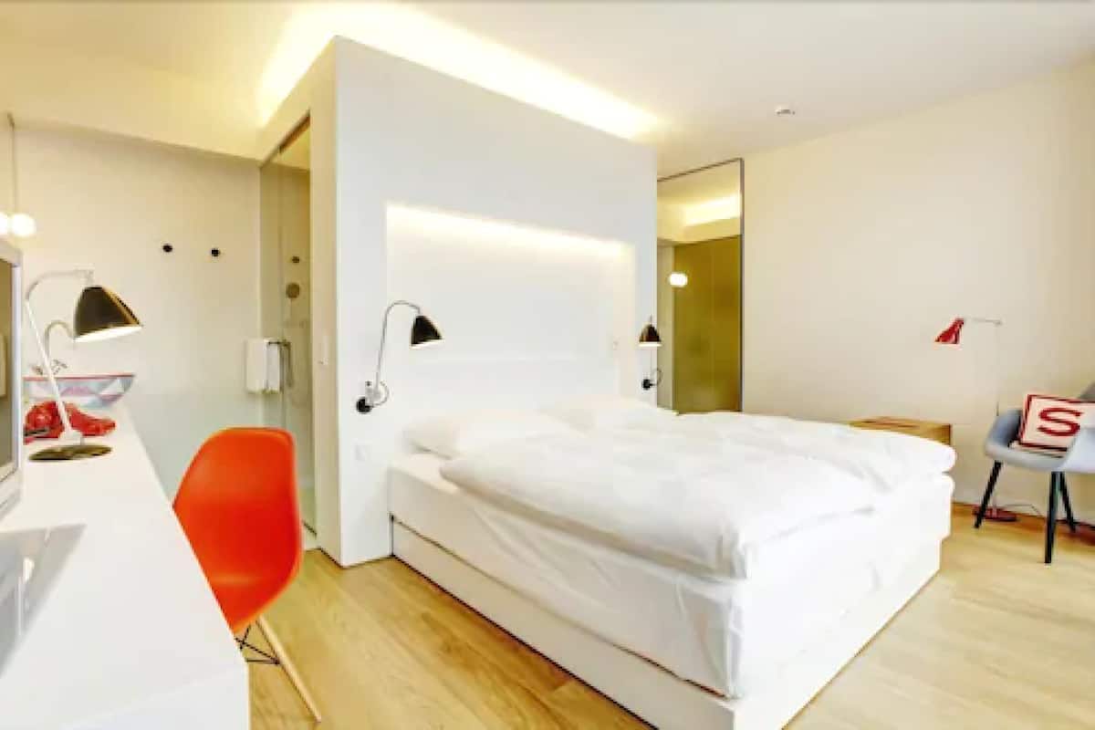 Moderni hotellihuone, jossa on sänky, työpöytä ja tuoli.