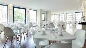 A spacious dining area with white tables and chairs, large windows, and a modern interior design. - Smartcity Designhotel (Hannover)