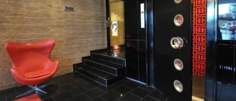 A modern lobby with a red chair, black tiled floor, and a staircase leading to an elevator.