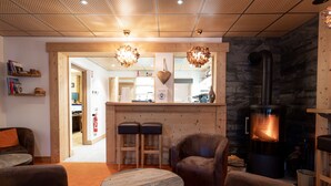 A cozy living room with leather sofas, a round wooden table, and a stone fireplace. There are two bar stools and a wooden counter in the background. - La Ferme du Lac (Thyez)