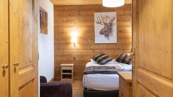 Een kamer met houten lambrisering, een bed, een nachtkastje, een lamp en een kunstwerk van een eland aan de muur.