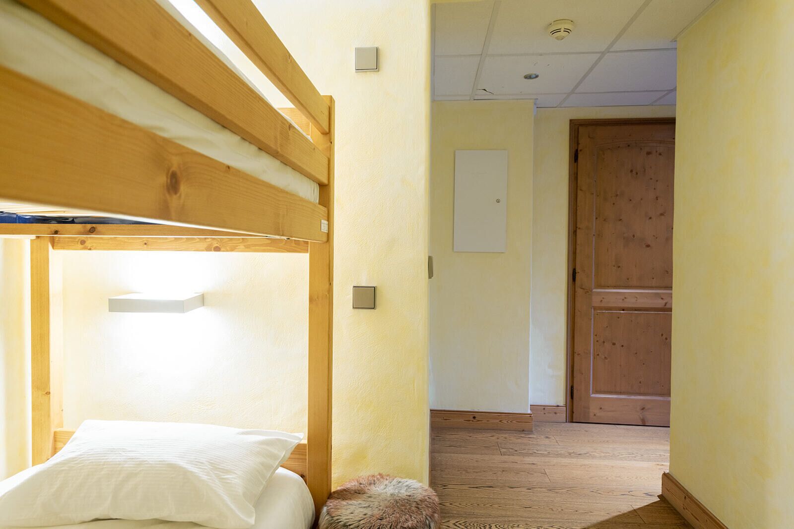 A bunk bed with a light fixture above it, a wooden door, and a white wall with a light switch.