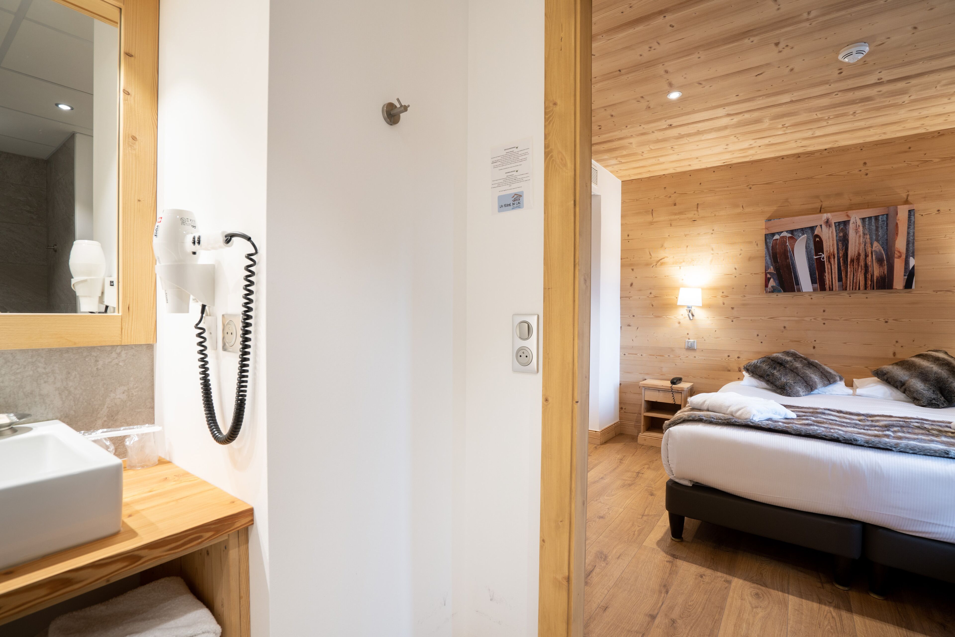 Un dormitorio con techo de madera, una cama con almohadas, una mesita de noche y un buró.