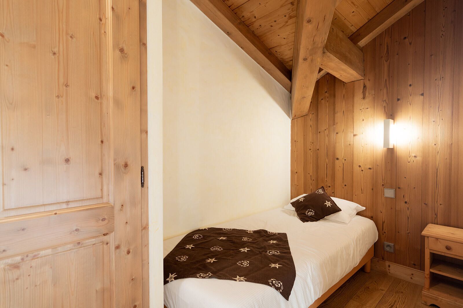 A wooden room with a bed, a nightstand, and a wall-mounted light fixture.