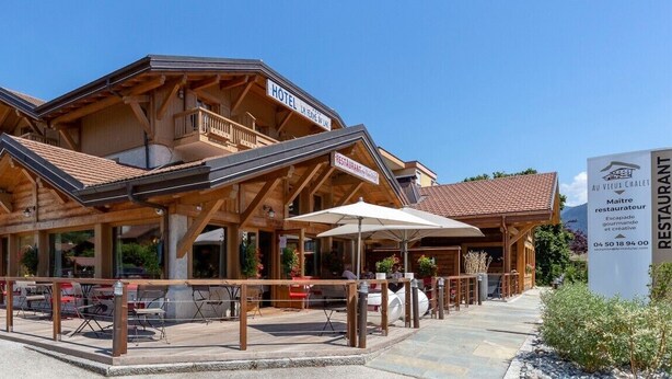 A wooden chalet-style building with a balcony, a restaurant sign, and outdoor seating. - La Ferme du Lac (Thyez)