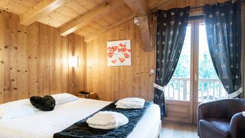 Ein Zimmer in einer Holzhütte mit einem Bett, einem Sessel und einem Fenster mit Vorhängen.