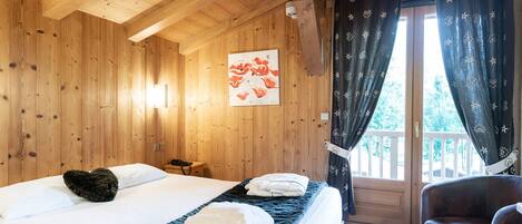 Ein Zimmer in einer Holzhütte mit einem Bett, einem Sessel und einem Fenster mit Vorhängen.