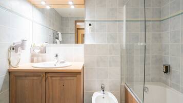 A modern bathroom with a wooden vanity, a sink, a bidet, and a glass shower enclosure.