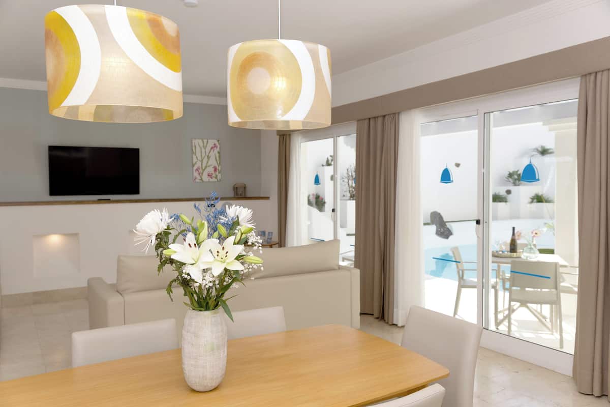 A modern living room with a sofa, a wooden table with a vase of flowers, and a television on the wall.