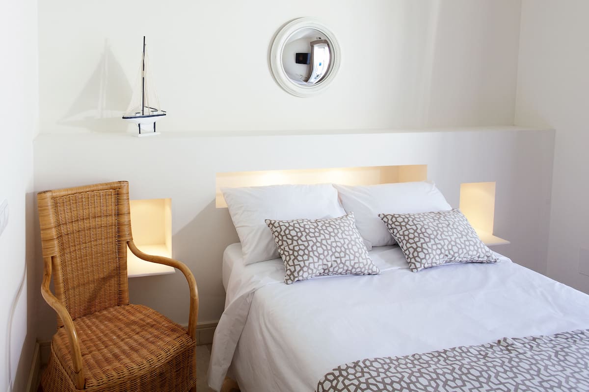 A hotel room with a bed, a chair, a wall-mounted mirror, and a small sailboat model.